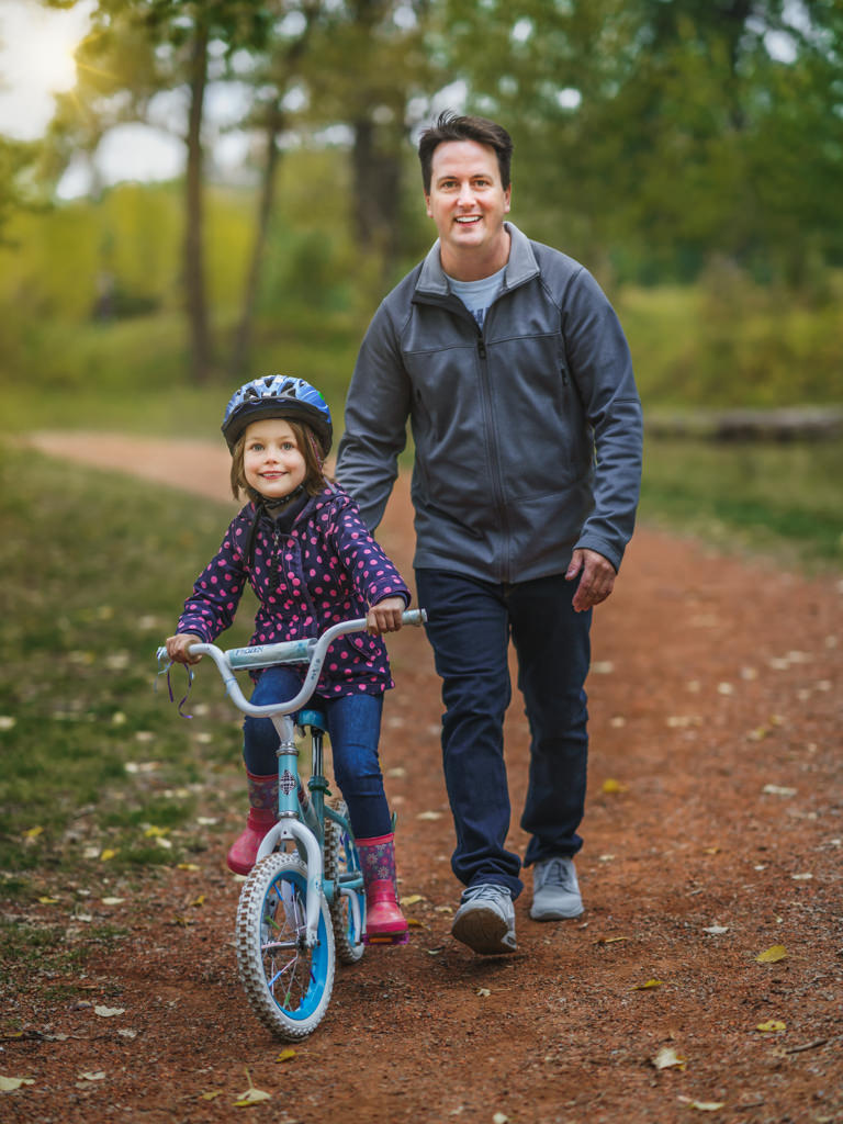 daughter riding bicycle with father behind her