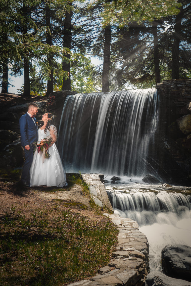 bride and groom posing against waterfall